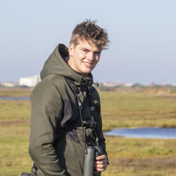 Bram Roobol kijkt lachend in camera met verrekijker om zijn nek